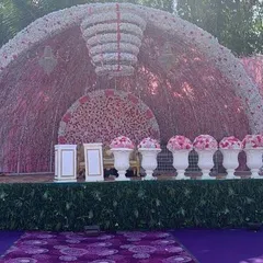 An incredibly grand and opulent reception stage. This magnificent structure is covered in thousands of pink and white flowers, featuring a large floral chandelier and elegant urns, creating a breathtaking backdrop.