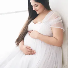 A gentle and intimate moment captured in soft, natural light. The mother-to-be is dressed in a delicate white tulle gown, creating a portrait that feels both peaceful and radiant.