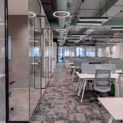 Glass-walled meeting rooms line the main corridor, reinforcing a culture of transparency. This design choice allows natural light to flow deep into the office floor plate while providing necessary acoustic privacy for meetings.