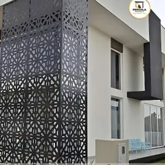 A corner of a modern villa is wrapped in a stunning black metal screen with a geometric, laser-cut pattern. This design element acts as both a decorative facade and a privacy screen, adding a bold, contemporary edge to the architecture.