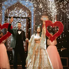 A grand entrance for the ring ceremony. The couple waves to their guests, framed by giant red hearts and a shower of sparkles, making for a truly memorable and celebratory photograph.