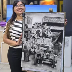 This student proudly presents her large-scale charcoal drawing, a complex scene filled with people and a vehicle, showcasing her storytelling ability.