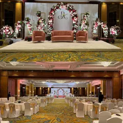 A full view of a ballroom setup, showing how the stage design with its floral arch and monogram integrates with the overall guest seating and venue architecture.