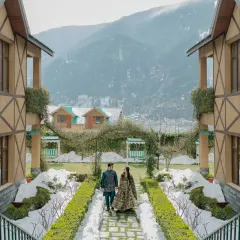 A winter fairytale in Manali. The couple walks down a snow lined path, the symmetrical architecture and mountain backdrop creating a scene straight out of a movie. This is a perfect example of a unique seasonal destination wedding.