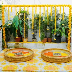 An elegant and simple Haldi setup for an intimate ceremony at home. We used a backdrop of marigold garlands against the home's natural greenery, with brass urlis filled with flower petals for the ritual.