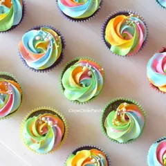 A close-up view of my rainbow swirl cupcakes. The chocolate cupcakes are topped with a multi-coloured buttercream frosting and a light dusting of white sprinkles.