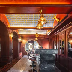 We designed this opulent home bar with rich mahogany wood paneling, a black marble countertop, and a stained-glass ceiling that mimics a blue sky. The space is reminiscent of a classic, exclusive club, perfect for entertaining.