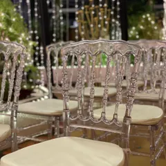 A close-up of the elegant transparent chairs. Their intricate design adds a touch of sophistication, especially when set against a curtain of warm, twinkling lights.