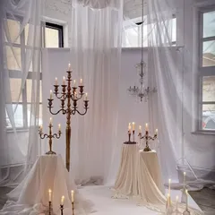 I create ethereal and romantic settings using sheer white fabrics and an abundance of candles. This setup, with its dramatic candelabras, is perfect for a pre-wedding shoot or an intimate ceremony.