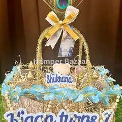 A close-up of the 'Kiaan turns 1' Shukrana hamper, featuring a golden basket, pearl details, and a peacock feather.