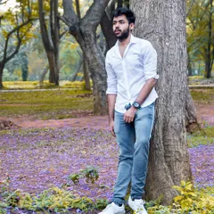 An environmental portrait of a man leaning against a tree in a park with purple flowers on the ground. The natural light and beautiful colors of the location add depth to the shot.