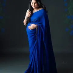 The deep, royal blue of this saree is simply captivating. We love how the soft studio light highlights the fabric's texture and the mom-to-be's gentle expression.