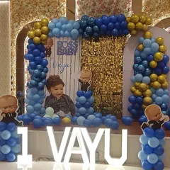 The Boss Baby theme is a huge hit for first birthdays. Here is a complete stage setup for Vayu's party in Noida, featuring a custom backdrop with his photo, character cutouts, and a blue and gold balloon arch, all tied together with large "1 VAYU" marquee letters.