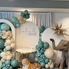 We bring wild adventures to life with our themed parties. This immersive jungle safari setup for a first birthday features lifelike animal props like a giraffe and elephant, set against custom arched backdrops and a lush balloon arrangement in sage green and neutral tones.