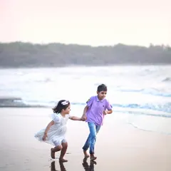 The pure joy of childhood captured in a single frame. Two siblings run freely on the beach, hand in hand, with the waves chasing their feet.