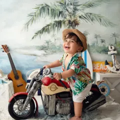 This little guy is having a blast during his beach-themed sitter session, laughing with joy as he "rides" a miniature motorcycle prop.