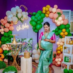 The mother-to-be stands before her beautiful baby shower decor, complete with a balloon arch and a "Oh Baby" neon sign. A perfect picture of the celebration.