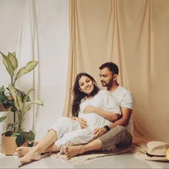 Dressed in simple whites against an earthy, neutral backdrop, this portrait captures a serene and natural moment of togetherness for the expecting couple.
