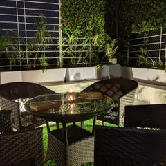 This is the finished balcony at night, a serene corner designed for quiet moments. The combination of wicker furniture, a soft artificial lawn, and a vertical plant wall creates a comfortable and intimate outdoor room.