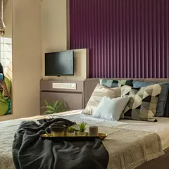 We created a cozy reading nook right by the window in this master bedroom. The design features a bold purple fluted panel behind the bed, which adds texture and a pop of color to the otherwise neutral space.