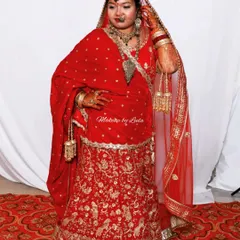 A stunning North Indian bride in a traditional red and gold lehenga. The makeup is bold and glamorous, complete with a maang tikka and a nose ring (nath).
