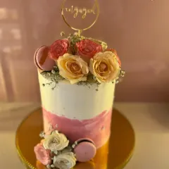 This chic and modern engagement cake features a smooth white and pink watercolor finish. It's adorned with fresh roses and delicate macarons, topped with a gold "Engaged" ring for a stylish celebration.