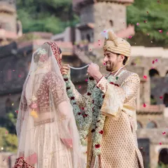 The jaimala moment at a royal fort wedding, with the groom playfully lifting the garland over the bride's head as petals rain down.
