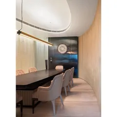 The curved wall continues into the conference room, creating a soft, enveloping space. A linear light fixture follows the line of the long table, providing focused illumination.