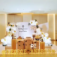 A full view of the First Holy Communion stage for George and Andrea. The asymmetrical design with balloon clouds, pedestals for cake and decor, and marquee lights creates a dynamic and modern look.