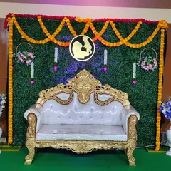 A full view of the green wall backdrop for a baby shower. It features an ornate gold and white sofa, marigold garlands, and a custom central motif, creating a traditional yet stylish look.