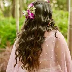 A back view of a gorgeous hairstyle for a Haldi ceremony. The long, loose curls are decorated with fresh orchids, tying the whole look together.