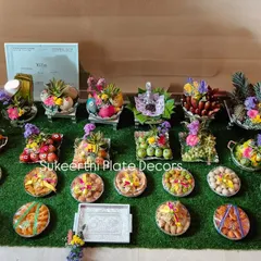 A beautiful and elaborate platter arrangement for a puberty ceremony in Hosur. This display features a wide variety of seer thattu, including fresh fruits like apples and grapes, sweets, and other traditional items, all decorated with care.