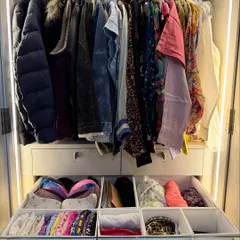 A wardrobe where hanging clothes are placed above drawers filled with neatly organized smaller items. The integrated lighting makes everything inside visible and accessible.