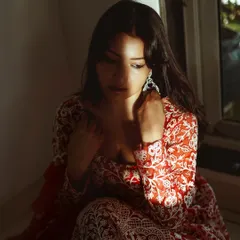 A quiet, introspective moment captured during the shoot. This photo highlights the intricate white embroidery on the red fabric of her traditional dress.