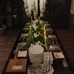 A dramatic, candlelit buffet setup for an evening event. The long table is adorned with white lilies and features a full spread in classic silver chafing dishes, creating a timeless and elegant look.