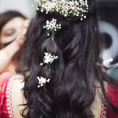 A detailed view of a romantic bridal hairstyle. This half-up style features soft waves and is adorned with delicate baby's breath, creating a look that is both elegant and effortless for an engagement or wedding day.