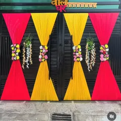 A simple and traditional decoration for the main gate of a wedding house. The gate is adorned with red and yellow drapes and floral bouquets to welcome guests.