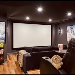 For spaces that blend daily life with entertainment, we design hybrid layouts like this one. It combines a comfortable sofa with a premium recliner, complete with movie posters and a snack cart to create a cozy, personalized cinema corner within a living area.