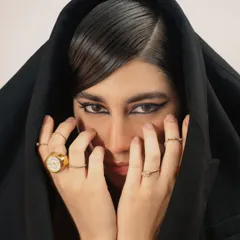 A dramatic beauty shot where a black hood frames the model's face. The focus is on the sharp, winged eyeliner and the statement rings, creating a mysterious and powerful image.