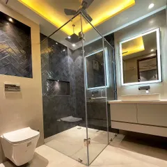 This bathroom features a dramatic walk-in shower with dark, glossy tiles laid in a chevron pattern. The space is illuminated with warm cove lighting in the ceiling and a backlit mirror over the vanity.