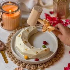 A hand poised with the hammer, ready to smash the Eid moon piñata. This image captures the anticipation and excitement of this unique dessert experience.