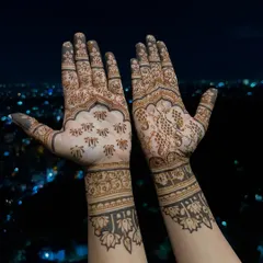 The palm-side view of Divya Spandana's mehendi, showing a mix of traditional butis and intricate floral work. One hand features a detailed peacock, while the other has scattered florals for a unique, asymmetrical style.