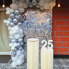 Celebrating a 25th birthday with a glamorous silver shimmer wall. The white and silver balloon arch and light-up marquee numbers add to the chic and festive atmosphere.