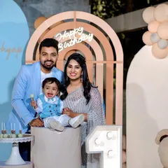 A happy family celebrating their son's first birthday with a modern teddy bear theme, featuring pastel blue and beige decor.