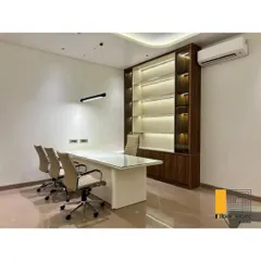 This executive office combines rich wood tones with modern, clean lines to create a space that feels both authoritative and stylish. The integrated back-lit shelving provides functional storage while adding a layer of ambient light and sophistication to the room.