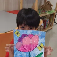 A shy artist peeking over his beautiful oil pastel drawing. We worked on blending techniques to create the soft petals of the tulip and the buzzing bees around it.