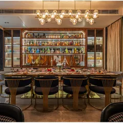 This stunning entertainment area features a dining table set against a custom, fully-stocked bar. The entire space overlooks the pool, with a tranquil water curtain feature that provides a soothing backdrop for any occasion.