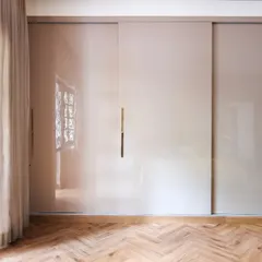 A simple yet elegant sliding wardrobe with acrylic glass shutters and rose gold concealed handles. The herringbone patterned wooden floor adds warmth and texture to this minimalist bedroom detail.