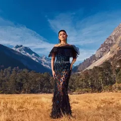 A dramatic editorial shot featuring a model in a stunning black gown against the majestic mountains of Arunachal Pradesh. Her hair is styled in a chic updo to accentuate her neckline and the dress's silhouette.