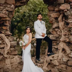 Karen and Abhijeet framed by a natural stone archway in Goa. This shot combines formal wedding attire with a rustic, historic location for a powerful, editorial-style portrait.